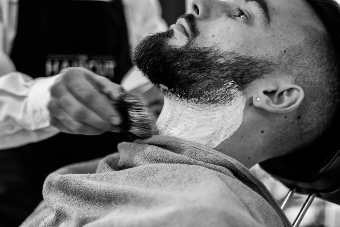 A barber meticulously trimming a man's beard with precision tools.